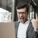Mężczyzna cieszący się z sukcesu przy laptopie – przykład, jak pisanie treści zgodnych z E-E-A-T wzmacnia SEO i widoczność w Google.