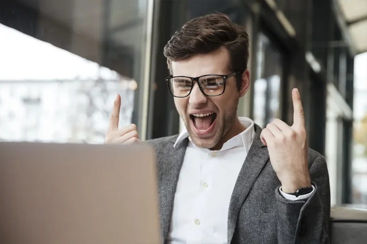 Mężczyzna cieszący się z sukcesu przy laptopie – przykład, jak pisanie treści zgodnych z E-E-A-T wzmacnia SEO i widoczność w Google.